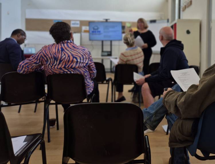 people sitting while someone stands at front speaking